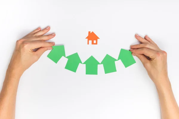 Hands holding green paper house figure models arrows on white background. Concept for comparision of real estate houses pricing Real Estate Concept. Top view, copy space. Eco house — Φωτογραφία Αρχείου