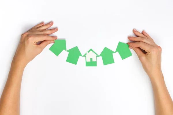 Hands hplding green paper house figure models arrows on white background. Concept for comparision of real estate houses pricing Real Estate Concept. Top view, copy space. Eco house