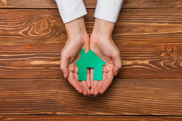Hands holding green paper house figure models arrows on white background. Concept for comparision of real estate houses pricing Real Estate Concept. Top view, copy space. Eco house — Stockfoto