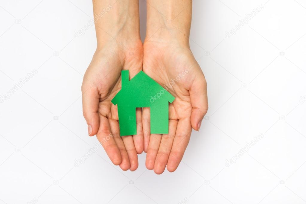 Hands hplding green paper house figure models arrows on white background. Concept for comparision of real estate houses pricing Real Estate Concept. Top view, copy space. Eco house