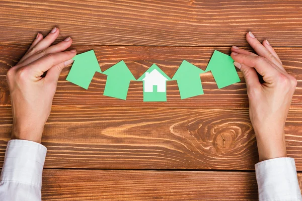 Hands hplding green paper house figure models arrows on grunge rustic wooden background. Concept for comparision of real estate houses pricing Real Estate Concept. Top view, copy space. Eco house — Stock Photo, Image