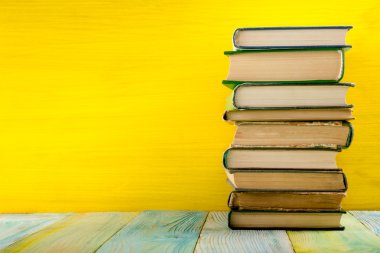 Stack of colorful hardback books on yellow background.