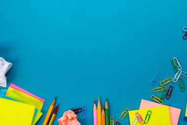 Ofis tablo Masası dizi renkli malzemeleri, beyaz boş not defteri, Kupası, kalem, pc, buruşuk kağıt, ile mavi arka plan üzerinde çiçek. Metin için en iyi görünüm ve kopya yer