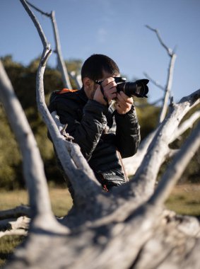 Fotoğrafçı, doğada bir ağacın yanında manzara fotoğrafları çekiyor.