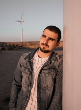 Sakallı adam gün batımını izlerken yel değirmenine yaslanıyor.