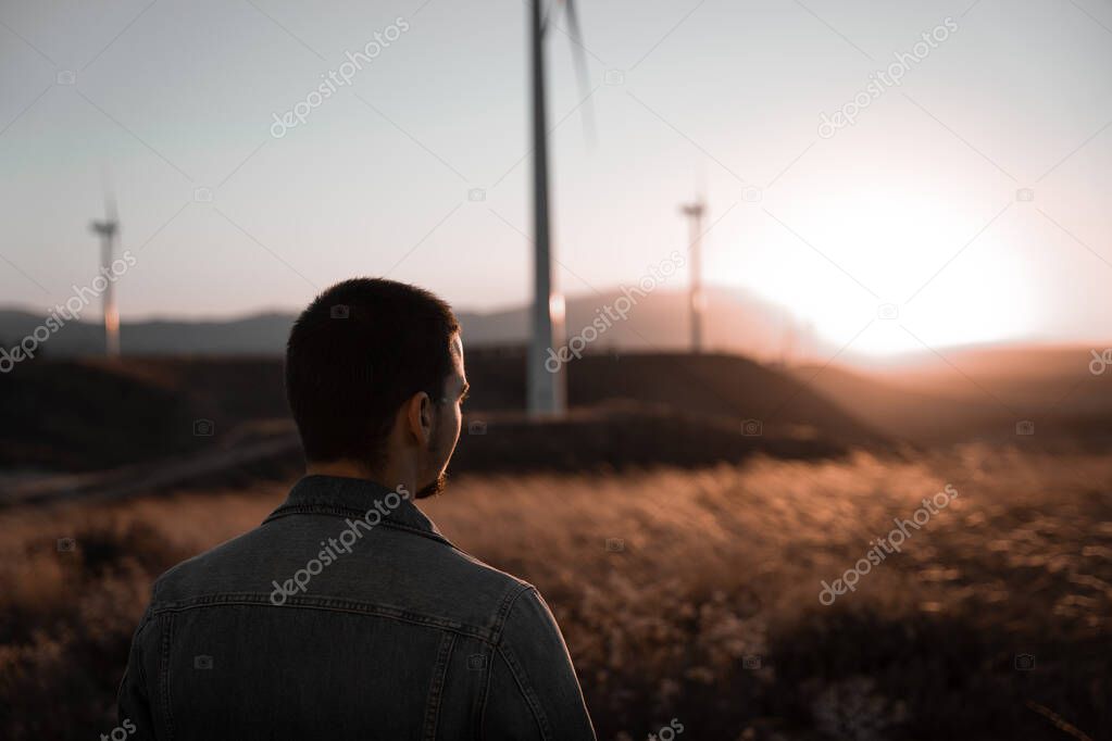 Man is thinking while watching the sunset surrounded by windmills