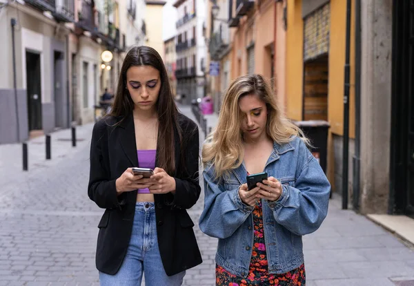 Şehir merkezinde yürürken telefonu kullanan iki kız.