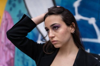 Esmer, genç bir kız model mavi bir duvar önünde gözleri kapalı poz veriyor.