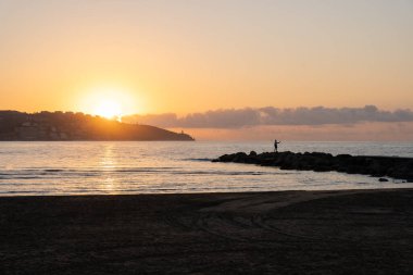 Sahilde gün doğumunda bir balıkçının siluetiyle