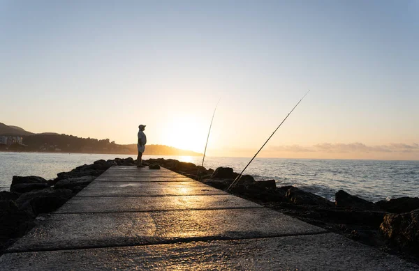 Silueta de viejo pescador junto a sus cañas de pescar durante el amanecer — Foto de Stock