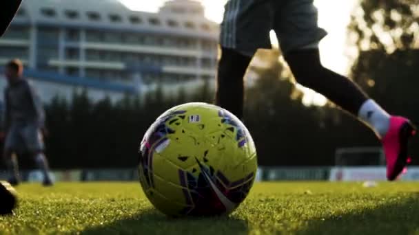 На футбольном поле футбольная команда бьет по мячу летящими всплесками в замедляющемся ярком солнце — стоковое видео