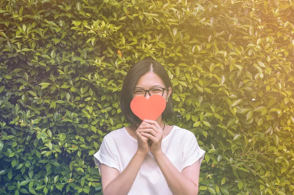 Asiática chica con gafas de ojo, sosteniendo un corazón de papel sobre fondo vegetal — Foto de Stock