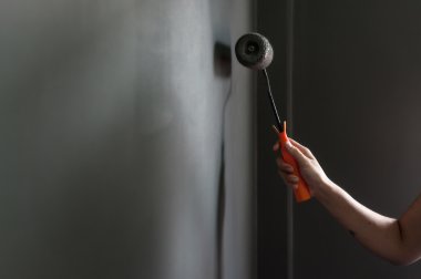 Gri boya uygulamak duvara boya silindiri tutan el. 