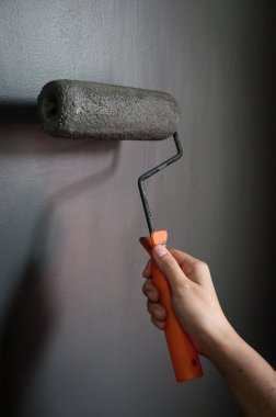 Duvara boya silindiri uygulanan gri boya kullanarak el yakın çekim.