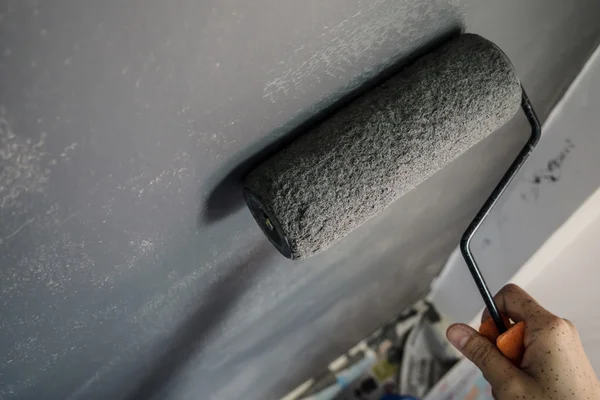 Close up de mão segurando rolo de pintura aplicando tinta cinza no wal — Fotografia de Stock