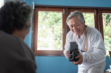 Asyalı ihtiyarın eski model fotoğraf makinesiyle karısının fotoğrafını çekerken portresi. Mutlu Boş Zamanlar evde kıdemli çift.