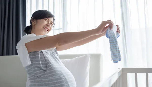 Feliz Sorrindo Asiático Grávida Mulher Embalagem Olhando Para Roupas Bebê — Fotografia de Stock