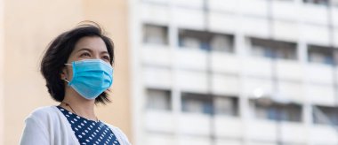 Koronavirüs ya da covid-19 salgını sırasında dışarıda koruyucu yüz maskesi takan Asyalı kadın..