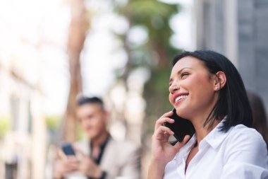 Açık havada konuşurken cep telefonu kullanan kendine güvenen İspanyol bir kadın. Gülümseyen güzel iş kadını akıllı telefon tutuyor..