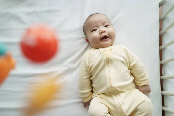Happy Smiling Asian Newborn baby boy lying on bed or cot having fun playing with colorful mobile.