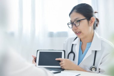 Asyalı kadın doktor veya hemşire hastanede tıbbi ekiple görüşmek için dijital tablet kullanıyor..
