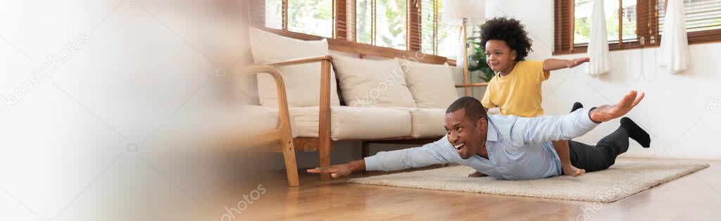 Happy African American Brazilian Father playing with Afro boy together. Black Dad pretend to be an aeroplane for his son on the floor.