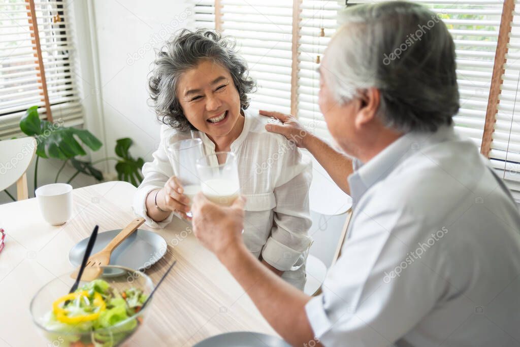 Happy Smiling Asian senior couple drinking glasses of milk at home together.