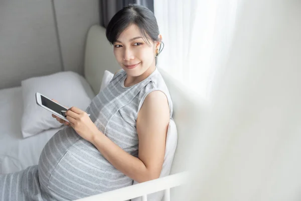 Sorrindo Jovem Mulher Grávida Asiática Usando Comprimido Digital Sentado Cama — Fotografia de Stock