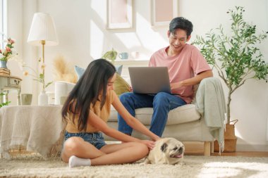 Mutlu Asyalı çift evde evcil köpekleriyle vakit geçiriyor. Adam dizüstü bilgisayarla gülerek sıcak bir yaşam tarzı yaratıyor..