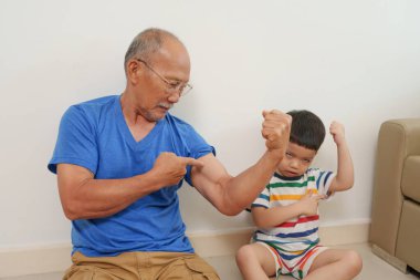 Neşeli Asyalı büyükbaba torunuyla içeride oynuyor, birlikte gülüyor ve kutluyor, neşe ve aile bağlarını ifade ediyor..