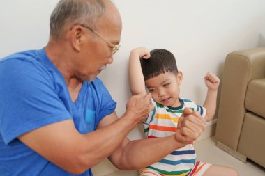 Mutlu Asyalı büyükbaba torunuyla kanepede eğleniyor. Evde gülümseme, şefkat ve sıcak aile ilişkilerini paylaşıyor..