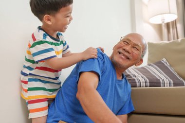 Mutlu Asyalı büyükbaba kanepede dinlenirken torunu onun yanında sarılıp şefkatini, şefkatini ve neşeli aile anını ifade ediyor..