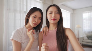 Güzel Asyalı arkadaşlar içeride poz veriyor ve gülümsüyor, rahat bir evde güven, mutluluk ve sıcak bir bağ ifade ediyorlar..