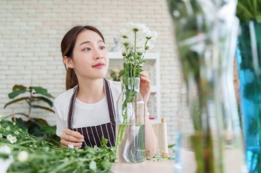 Çiçeklerle dikkatli çalışan Asyalı kadın çiçekçi, vazoda buket düzenliyor ve huzurlu yaratıcı anın tadını çıkarıyor..