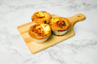 Mermer masada ahşap tahtaya dizilmiş üç tane yeni pişmiş yumurtalı tart resmi. 