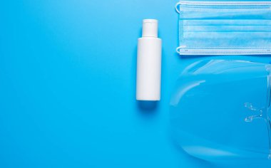 Mavi arka planda yüz maskesi ve el dezenfektanı resmi. Covid-19 salgını sırasında yüz kalkanına ihtiyaç duyulur ve takılması önerilir.