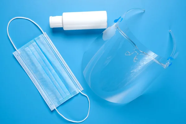 A picture of face shield mask and hand sanitizer on blue background. It is advised to wear during Covid-19 outbreak.