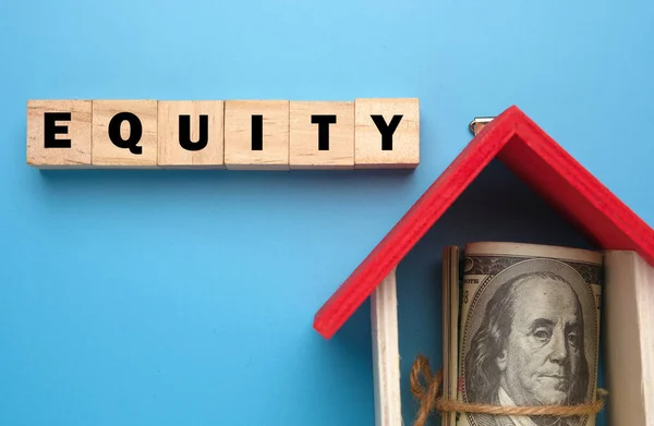 A picture of wooden block with Equity word, house miniature and fake money insight. Equity is the difference between the market value of your home and the amount you owe the lender who holds the mortgage