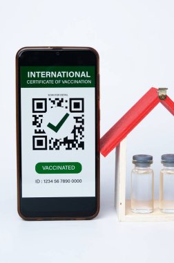 Üzerinde sahte Uluslararası Aşı Sertifikası olan bir akıllı telefon resmi. Ayrıca Covid-19 aşısı ve ev minyatür içgörü.