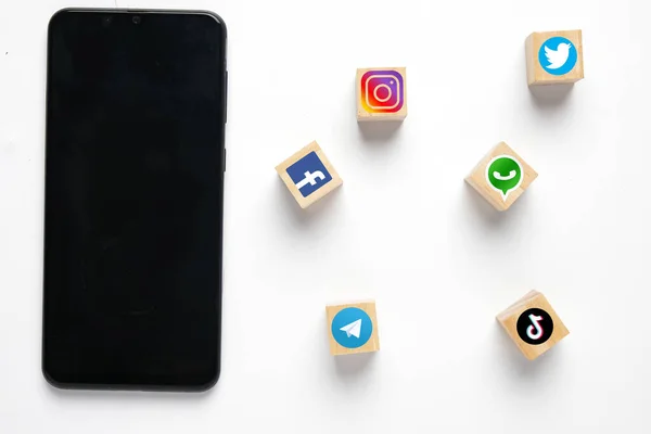 Ahşap blokta sosyal medya sembollü akıllı telefon. Sosyal medya aracılığıyla bizimle iletişime geçin..