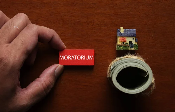A picture of house miniature, house insight and red wooden block written MORATORIUM. Moratorium is a length of time during which you enjoy a holiday from loan.