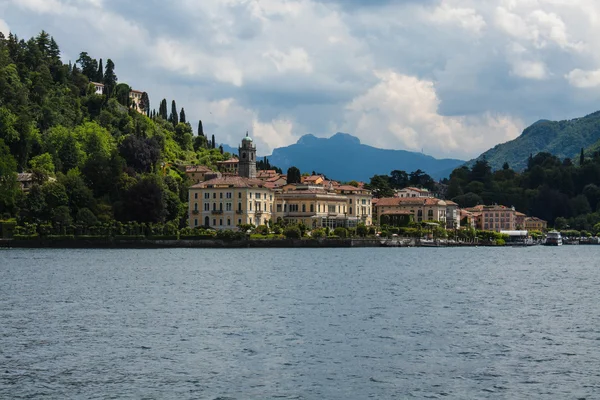 Vista de la línea de costa del Lago de Como, Italia, región de Lombardía. Paisaje italiano, con la montaña y la ciudad con muchos edificios de colores en la orilla — Foto de Stock