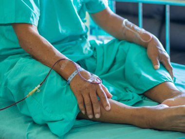 Üst düzey bir hastanın eli, hastada anemi tedavisi sırasında kan veriyor. Hastanede yatağında oturan Asyalı yaşlı bir hasta. Sağlık hizmetleri danışmanı