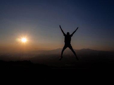 Genç adam gün batımında siluet şeklinde zıplıyor..