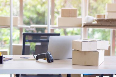 Ofisteki çalışma masasında bir dizüstü bilgisayar, ambalaj kutusu ve barkod okuyucu var. Müşterilerin siparişlerini çevrimiçi kanallardan hazırlıyorlar. Kolay bir girişim girişimcisi. E-ticaret kavramı. Metin için boşluk.