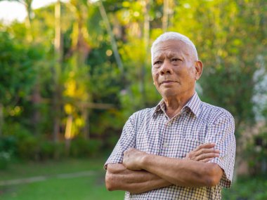 Bir bahçede dikilirken kollarını kavuşturup bakışlarını kaçıran yaşlı adamın portresi. Mesaj için yer var. Yaşlılar ve sağlık hizmetleri kavramı