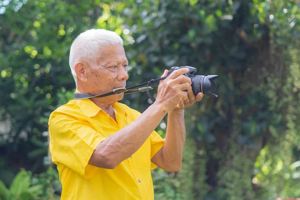 Son sınıf öğrencisi parkta dikilirken dijital kamerayla fotoğraf çekiyor. Yaşlı bir Asyalı adam sarı bir gömlek giyerse kamera kullanırken mutlu olur. Yaşlılar ve fotoğrafçılık kavramı