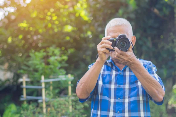 Son sınıf öğrencisi parkta dikilirken dijital kamerayla fotoğraf çekiyor. Yaşlı bir Asyalı adam mavi gömlek giyerse kamera kullanırken mutlu olur. Yaşlılar ve fotoğrafçılık kavramı