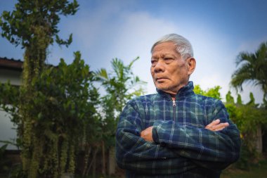 Yaşlı Asyalı adamın kolları çapraz bağlanmış ve bahçede dikilirken başka tarafa bakan portresi. Mesaj için yer var. Yaşlılar ve sağlık hizmetleri kavramı.