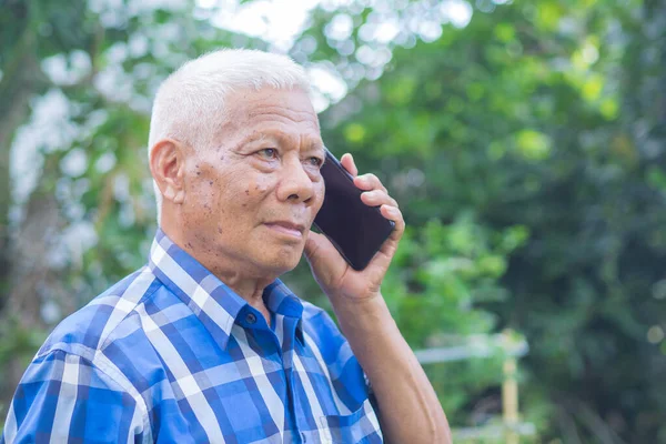 Senior man using a smartphone while standing in a garden. Space for text. Concept of aged people and technology.